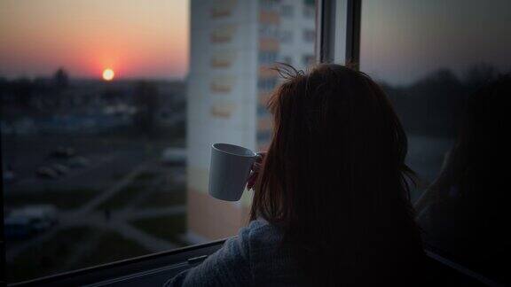 日落时分在阳台上喝咖啡的女人