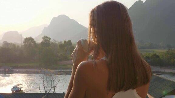 年轻女子在美丽的山景阳台上喝着热咖啡