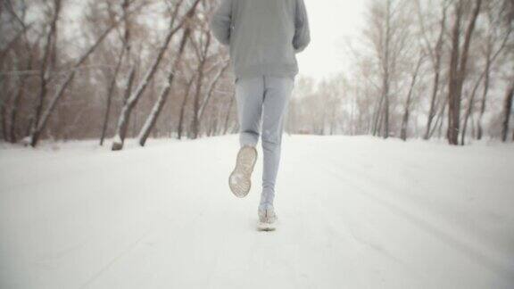 在冬季公园运动员的双腿穿着运动服和运动鞋奔跑背影特写一名男子在下雪时在冬季公园慢跑健康的生活方式概念