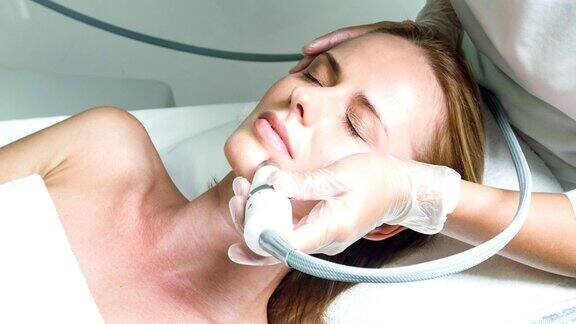 熟练的美容师用专用设备治疗女性面部