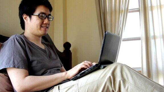 戴眼镜的快乐男人在床上用笔记本电脑在线聊天或视频会议