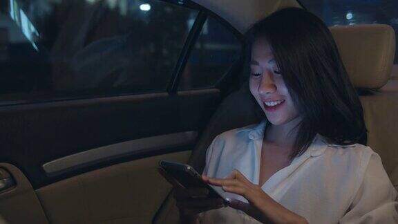 亚洲女商人穿着时尚的办公室服装工作到很晚在城市现代城市的汽车后座上使用智能手机