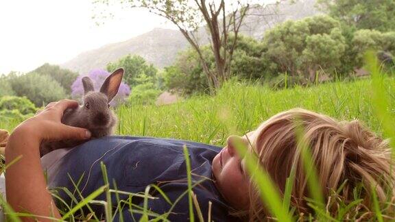 男孩喜欢他的小兔子躺在外面的草地上