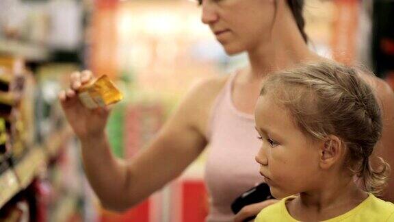 母亲带着小女儿在超市的糖果区挑选零食