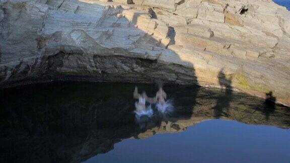 两个穿着比基尼的年轻女子一起从岩石上跳入水中