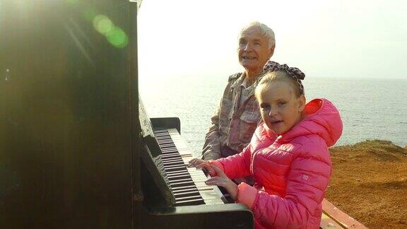 老人和小女孩在岸边的一架旧钢琴上一起弹奏