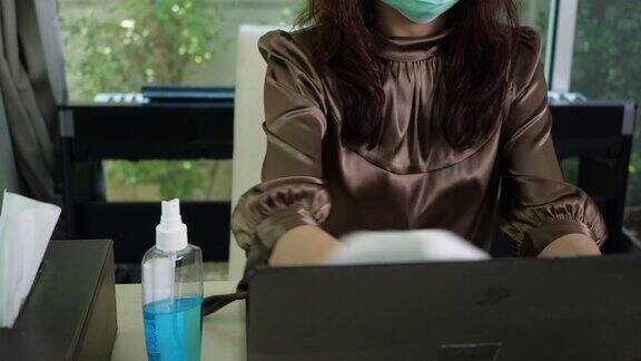 恐慌亚洲妇女戴着手套喷洒酒精清洁笔记本电脑以防止冠状病毒