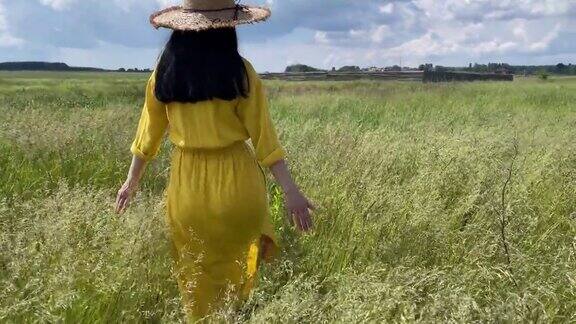 女孩戴着草帽穿着长裙走在绿色的夏日草地上
