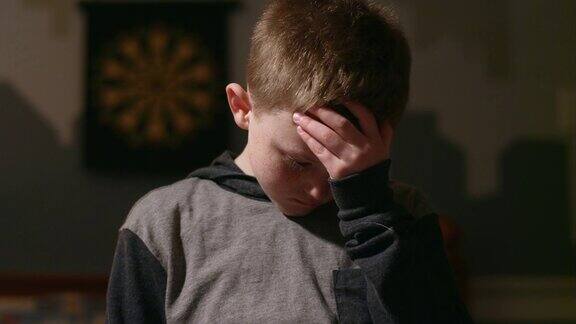 悲伤的小男孩站在自己的房间里双手抱头向下看