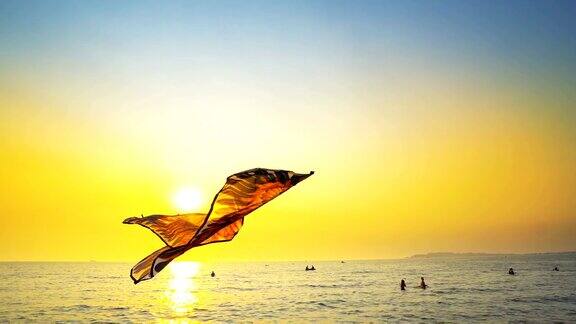 好玩的风筝玩具飞在海滩上反对夏天日落的太阳