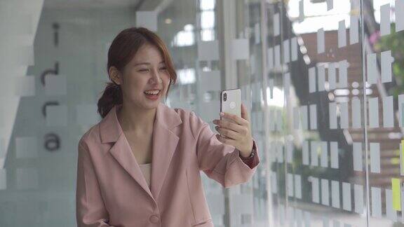 快乐的亚洲妇女视频呼叫微笑挥手的朋友使用智能手机互联网通信