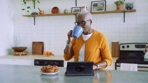 一位年长的女士一边在厨房吃早餐一边在她的平板电脑上工作