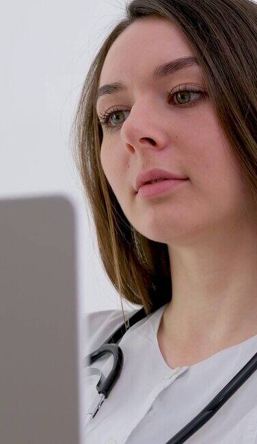 女医疗助理穿着白大褂戴着耳机在笔记本电脑上给远处的病人打电话医生使用虚拟聊天计算机应用程序与客户交谈远程医疗远程医疗服务概念
