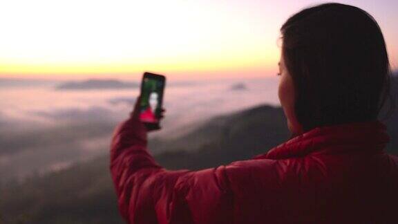 在有阳光和雾的山上拍摄风景的年轻女子的剪影带着相机独自旅行的背包客假日旅游和度假概念