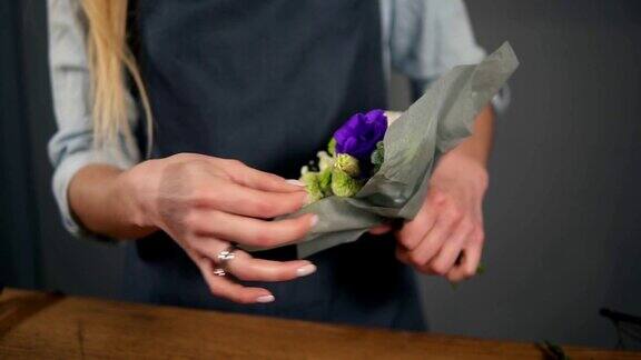 女性花商的手在装饰纸包裹一束花的特写视图Slowmotion拍摄