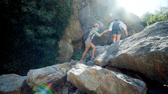 一个女旅行者在帮助她的朋友爬岩石