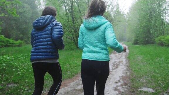 在雨中锻炼一对情侣在大雨中在绿树环绕的公园里跑步