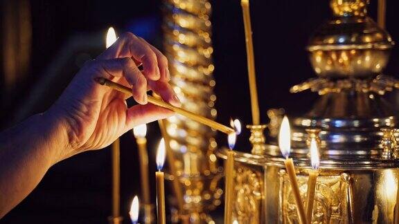 一个女人的手点燃了一支蜡烛把它放在教堂里的其他蜡烛中间