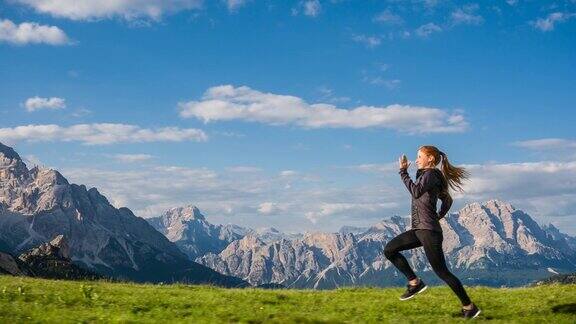 一个快乐的女人在草地上慢跑背景是山脉