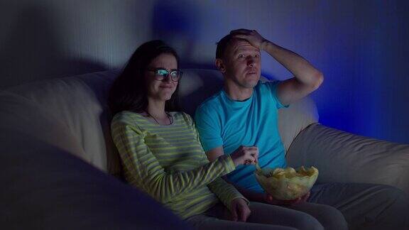一个男人和一个女孩一起看恶心的节目吃着薯片晚上坐在沙发上看电视