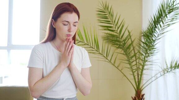 一个年轻女子在家里或室内交叉双臂真诚祈祷的特写白人女孩或女性真诚的祈祷