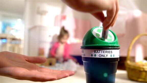 女性将用过的电池放入家里专门的回收箱孩子在背景上玩耍电池慢动作