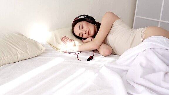 穿着内衣的女人躺在卧室里听着耳机里的音乐