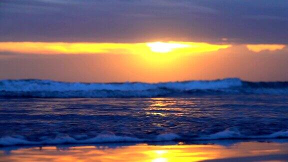 特写:蓝色的泡沫海浪冲刷沙滩在戏剧性的金色日落