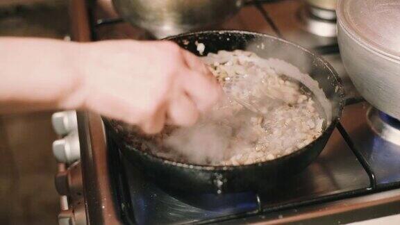 一个女人在厨房的铸铁煎锅上煎蘑菇和洋葱