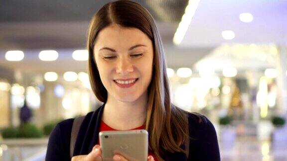 年轻美丽的女人走在购物中心微笑用她的智能手机和朋友聊天