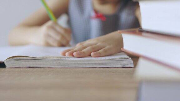 以一叠书为前景严肃地在桌上纸书上写字的女孩的手的正面和特写它体现了教育发展的专注学习的理念