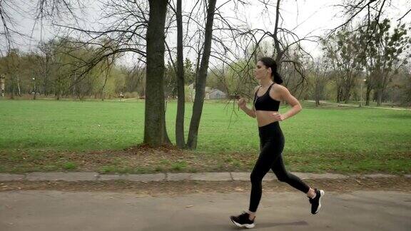 年轻的健康女孩戴着耳机在公园里跑步健康的生活方式运动理念侧视图