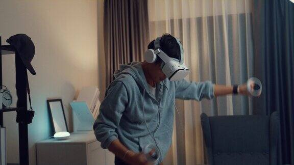 年轻的亚洲男子玩家穿灰色卫衣与VRoculus持有VR操纵杆控制器感觉激动与游戏的新体验站前沙发客厅在晚上的家