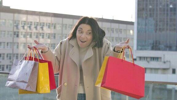 一幅惊讶的白人妇女举起彩色购物袋微笑的肖像成年女性购物狂站在城市街道上买东西Shopaholism生活方式电影4kProRes总部