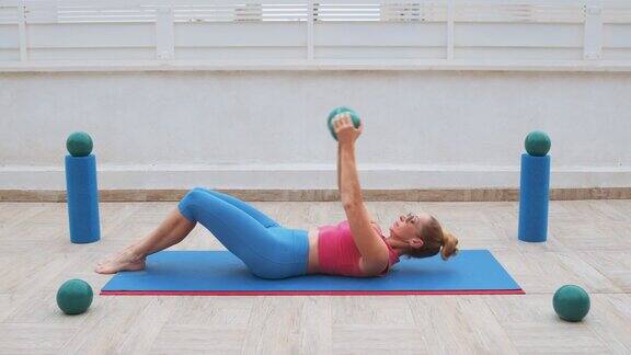 健身妇女做腹肌仰卧起坐和举起运动球在运动垫上