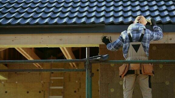 30多岁的屋顶工人在脚手架上检查陶瓷屋顶瓦的安装