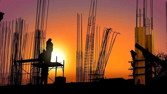 日落时分在一处建筑工地工人们在金属框架后面用铁丝将杆子固定在钢筋混凝土支柱的底部