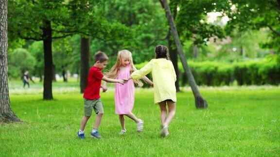 三个快乐无忧无虑的孩子在夏季公园的绿草地上手拉手跳舞