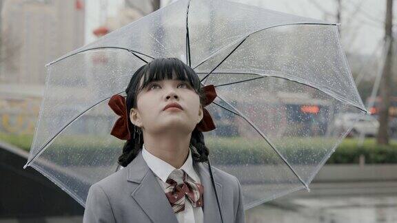 日本女学生穿着校服打着透明的雨伞站在雨中