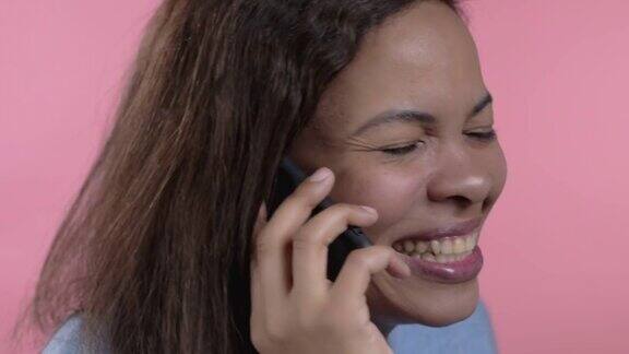 一个非洲女人在用手机说话混血女士拿着并使用智能手机粉红色的工作室背景