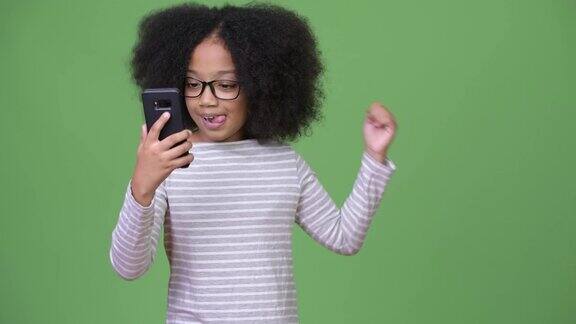 年轻可爱的非洲女孩与非洲发型使用电话和庆祝