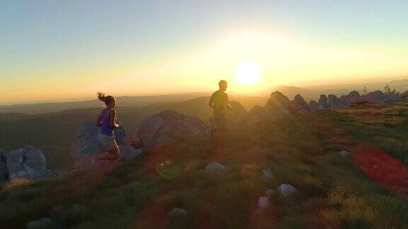 日落时分在一对在山间小道跑步的运动游客身后飞行