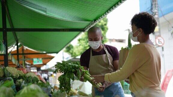 小贩戴着口罩向顾客展示蔬菜