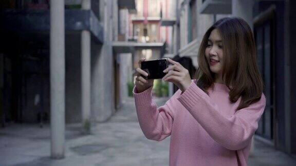 慢动作-年轻的亚洲女博主在城市里旅行美丽的女游客在假期用智能手机拍照生活方式女人在城市概念放松