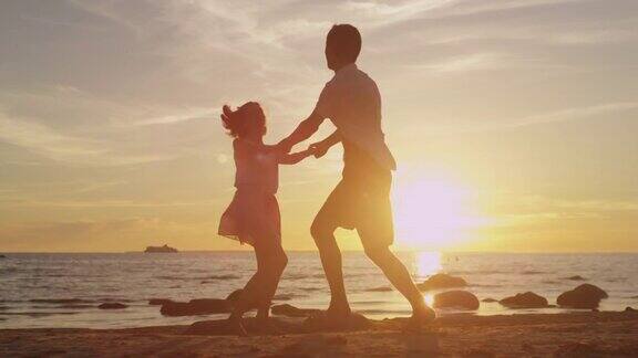 女孩和男人在沙滩上一起玩手牵着手在夕阳中旋转