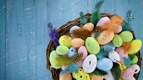 复活节彩蛋在一个巢与彩色羽毛转向蓝色木制背景