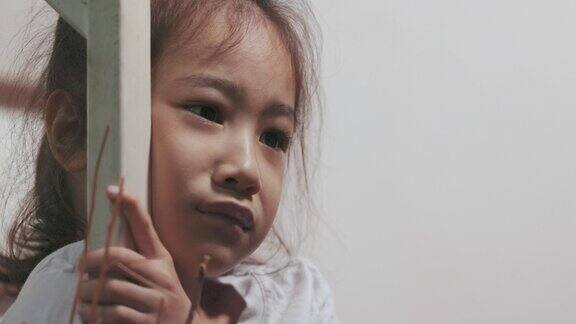 一个可爱的亚洲女孩独自在房子楼梯上表达她的悲伤情绪的特写脸显示了可能由于家庭和学校的抑郁情感上的痛苦和不快乐的孩子