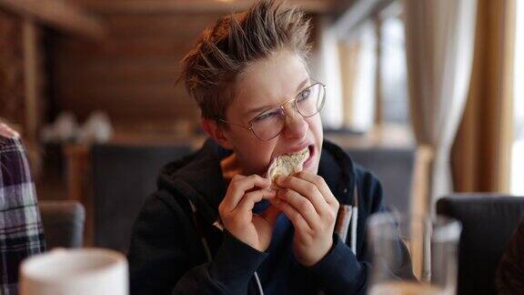 一个十几岁的男孩在吃一个很硬的三明治