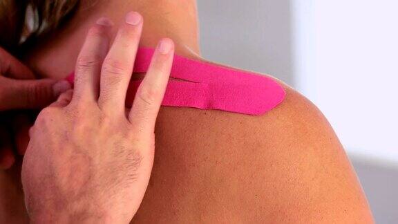 理疗师将粉红色的肌内肌贴贴在病人的背部