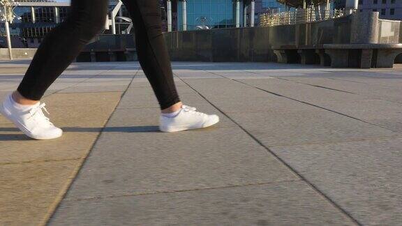 穿着白鞋的女人的腿走在干净、空旷的人行道上